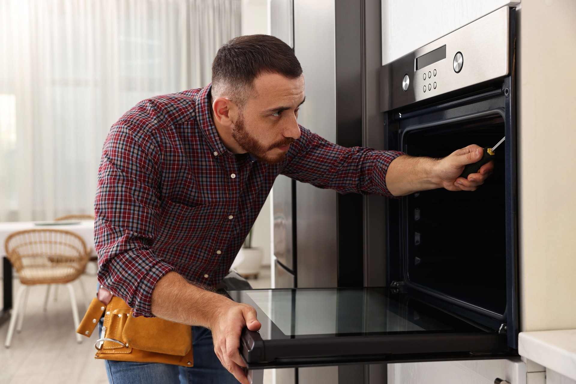 Repairman with screwdriver fixing oven at home